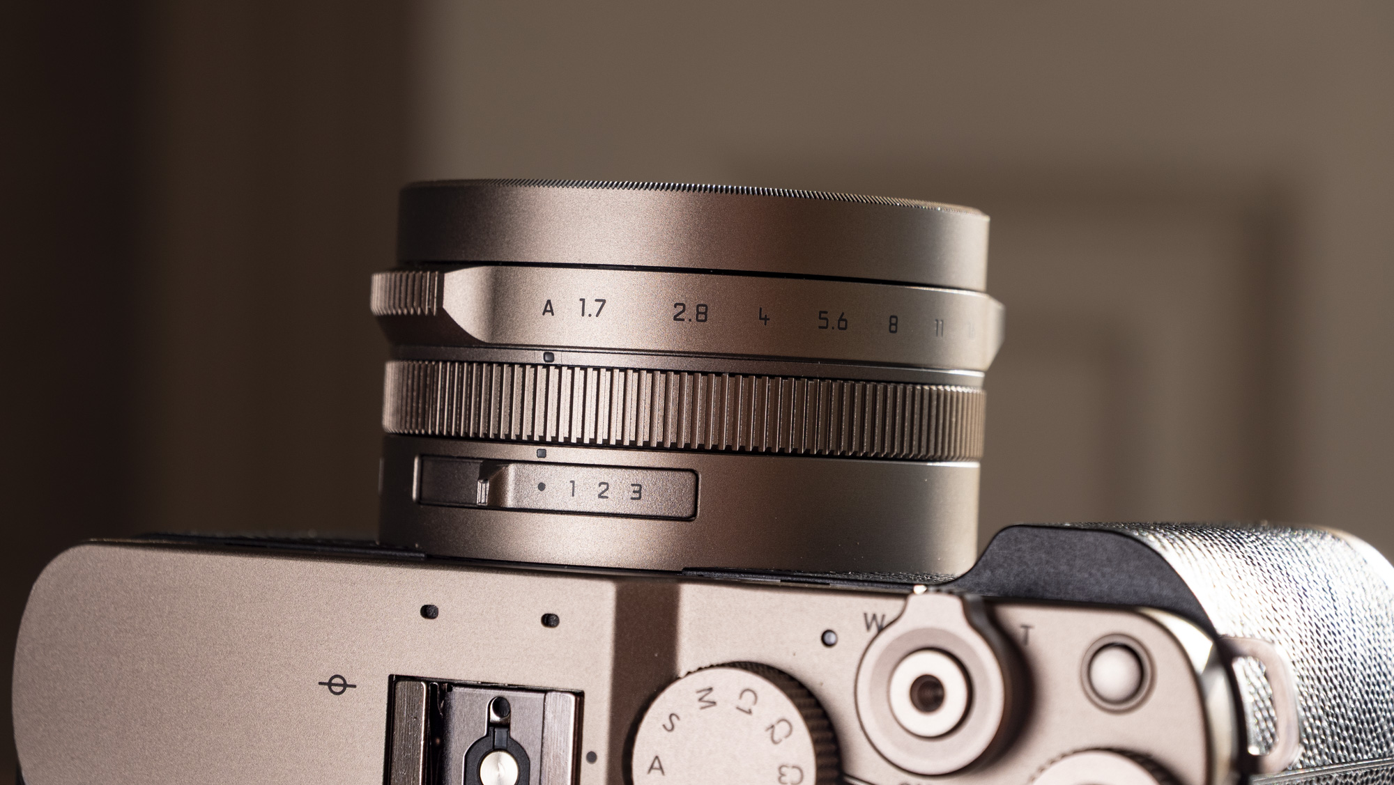 Close up of the lens of the Titanium Gold special edition of the Panasonic Lumix L10 compact camera, on an antique wooden table 