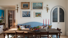 Dining room with a long mahogany table and chairs, a blue banquette, a gallery wall of vintage pictures, and antique candlesticks and sconces