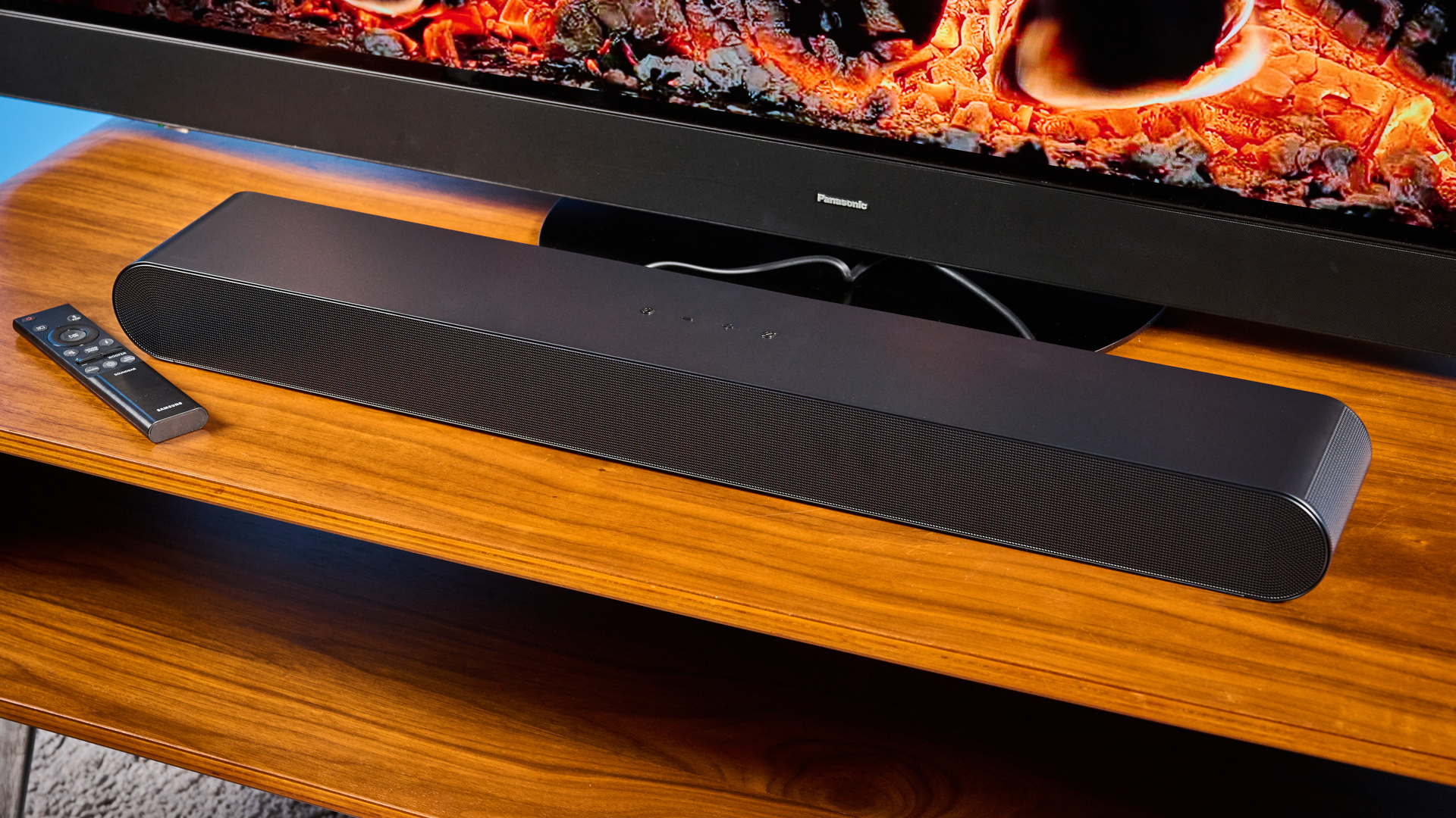 the samsung hw-s60D soundbar photographed on a wooden coffee table with a panasonic tv and a samsung soundbar against a blue background