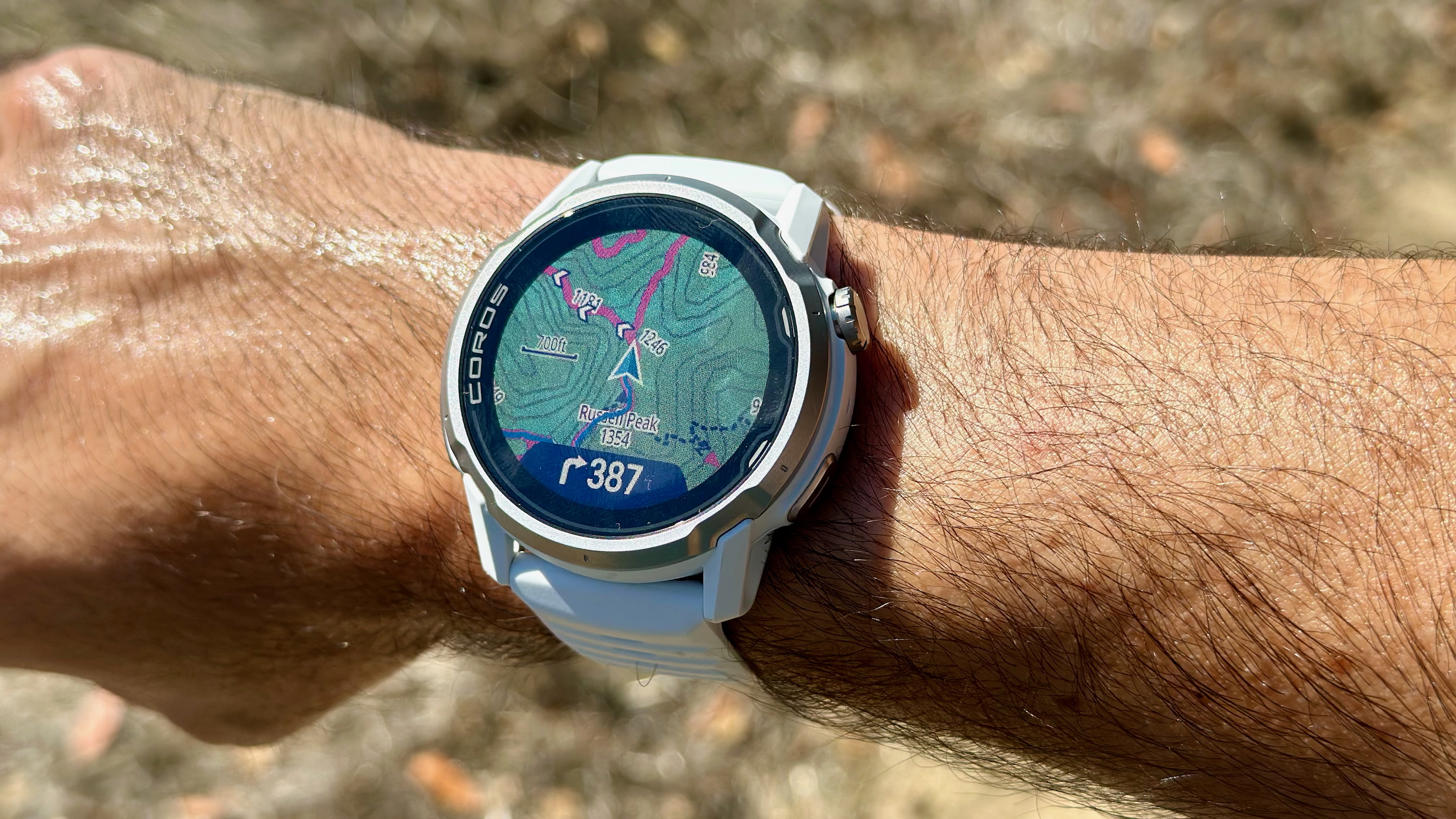 A photo of the COROS APEX 4 on the author's wrist showing a topographic map with turn-by-turn navigation showing a right turn in 387 feet.