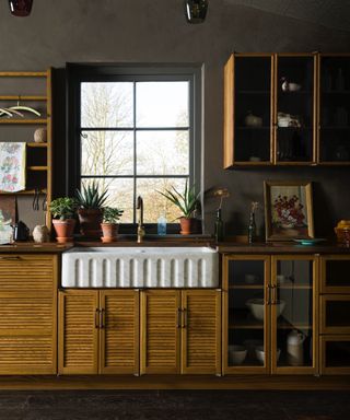 brown kitchen with fluted wood cabinetry, glazed units below and on walls, fluted sink, brass faucet, tea towels, plants