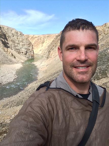 close-up selfie of jeremy hansen in outdoor clothing. behind him is a crater wall and a river