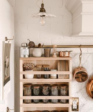 An image of a wooden storage rack mounted on a wall and filled with jars of dry ingredients