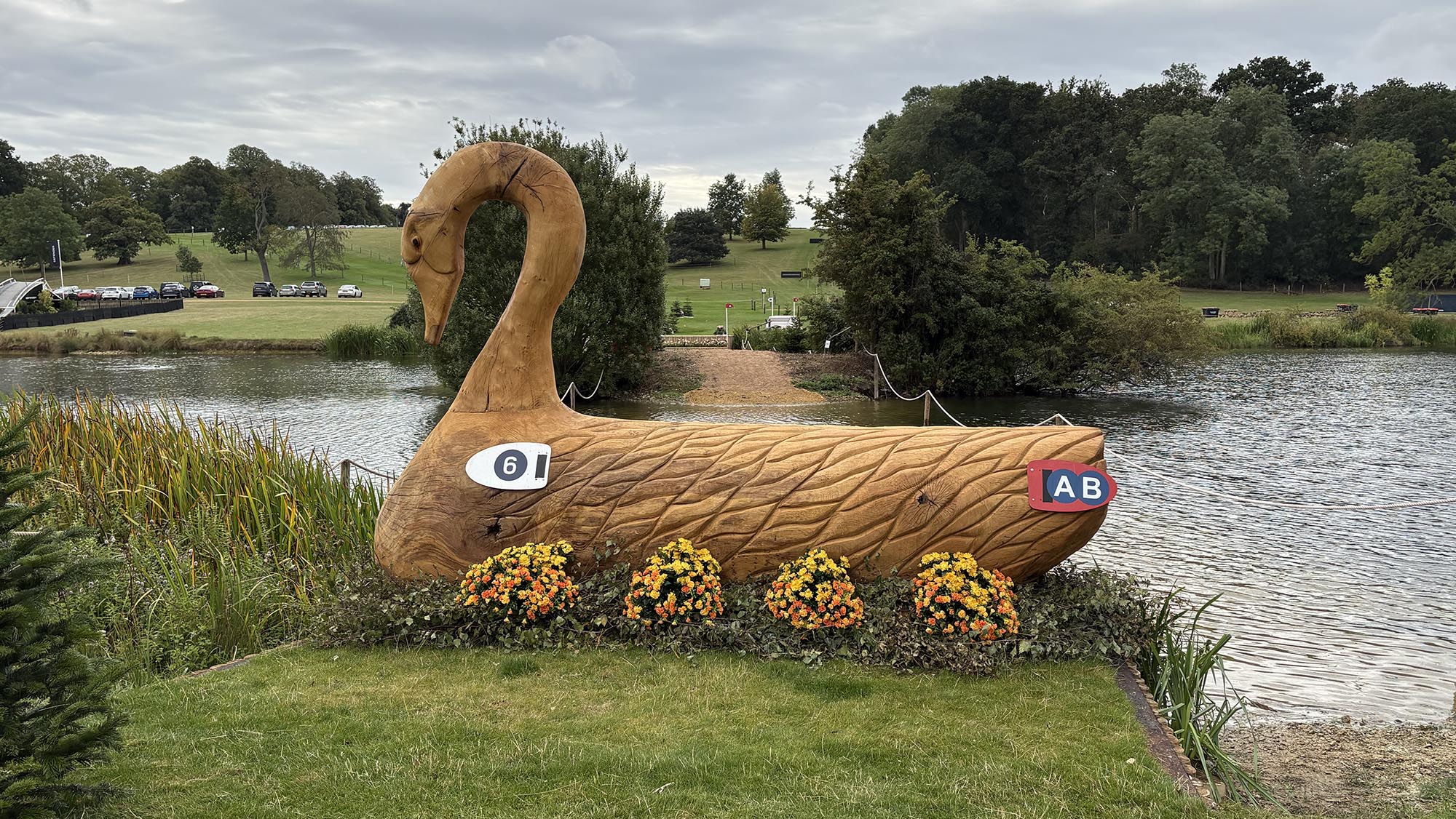 Wooden fence carved like a swan with water behind, on the Burghley cross-country course 2026