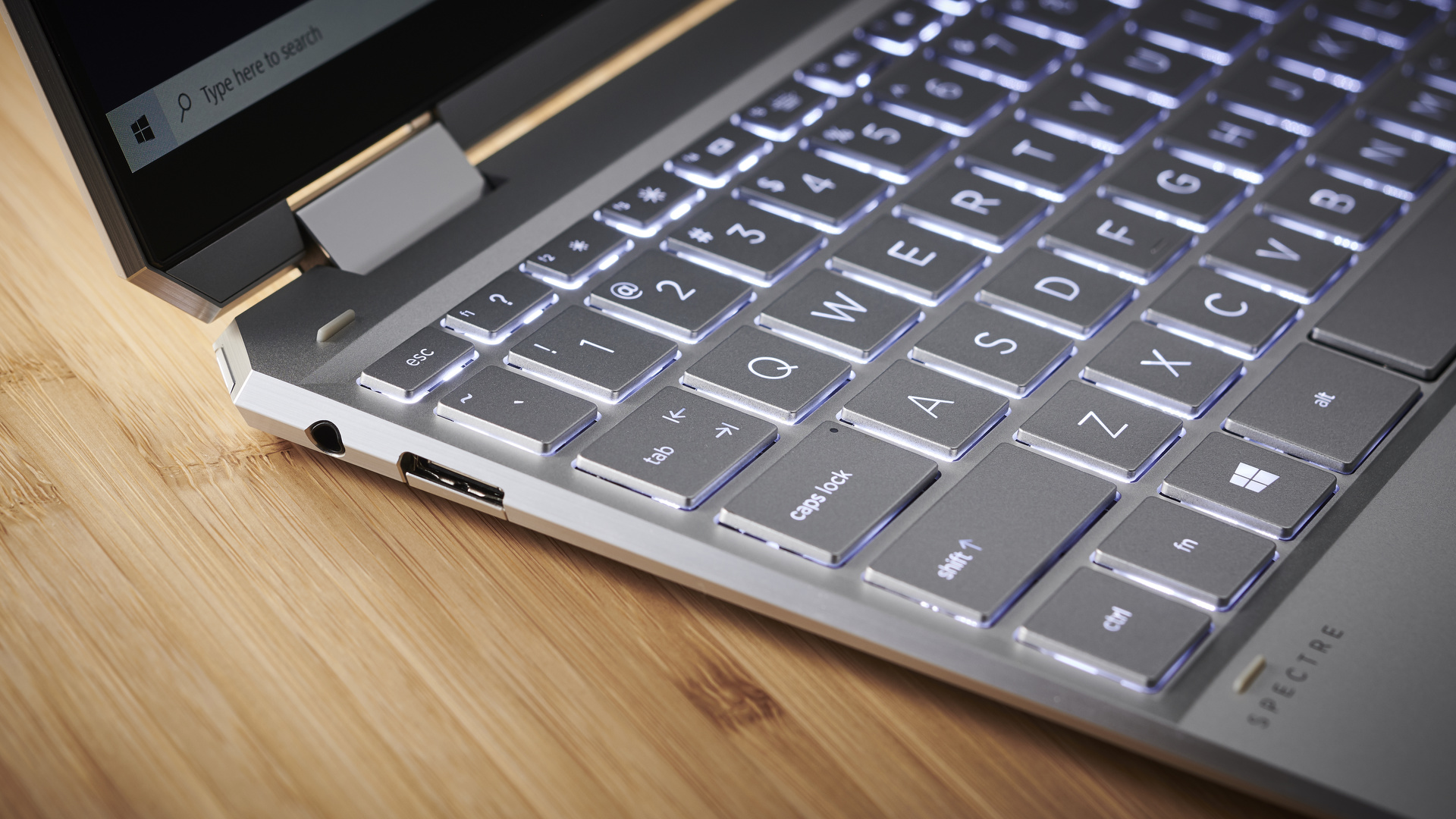 HP Spectre x360 (2021) on a wooden desk showing off its ports and part of its keyboard