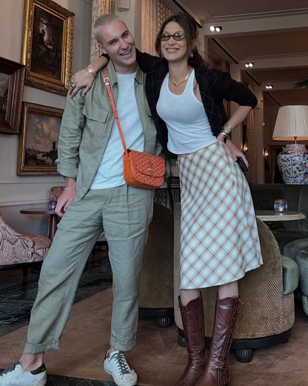 Bella Hadid poses with a friend wearing a knee-length skirt with knee-high boots with a tank-top and cardigan.