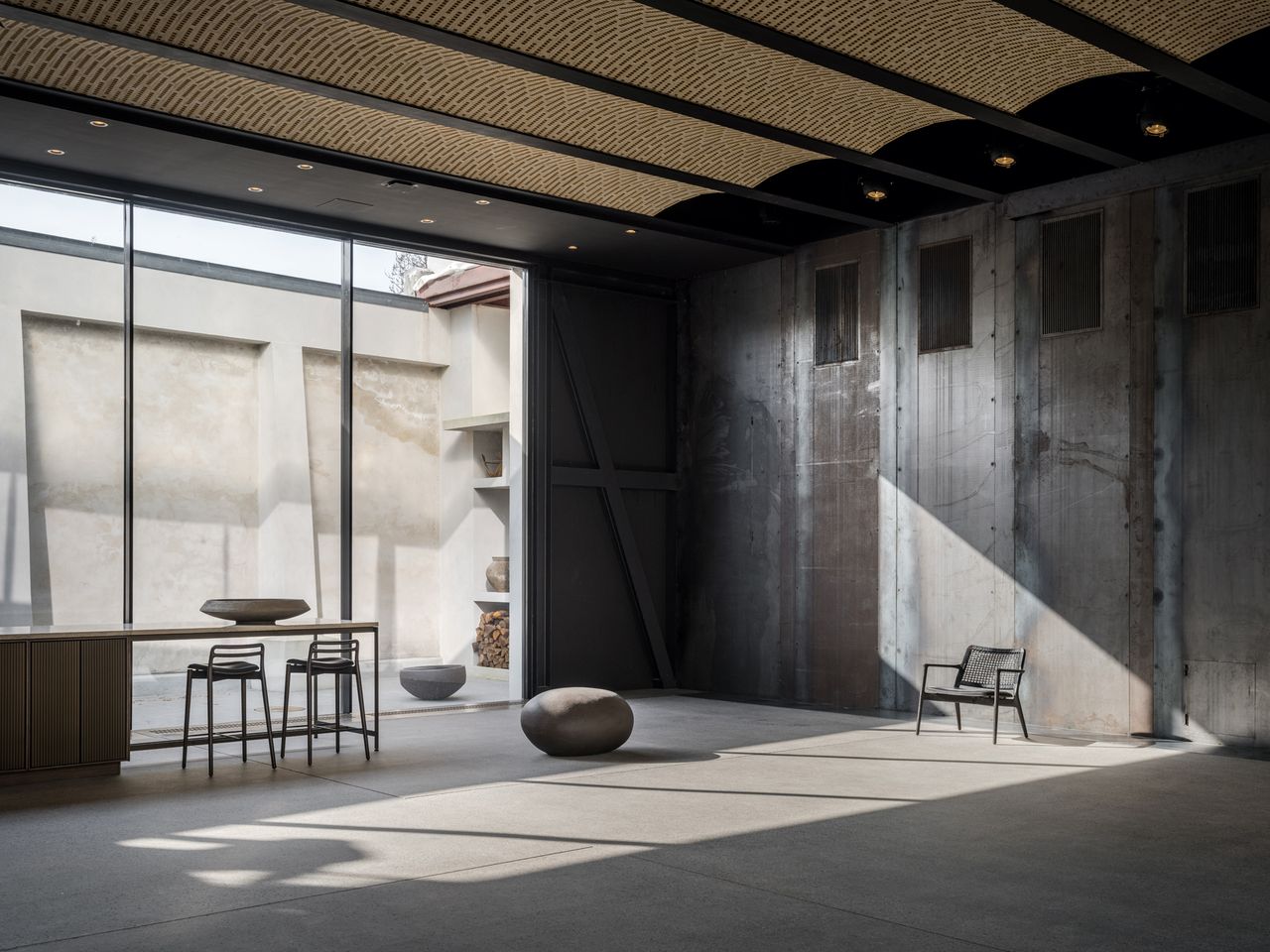 All-concrete room with an extended countertop area with two bar chairs next to the floor-to-ceiling windows.