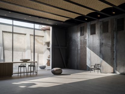 All-concrete room with an extended countertop area with two bar chairs next to the floor-to-ceiling windows.