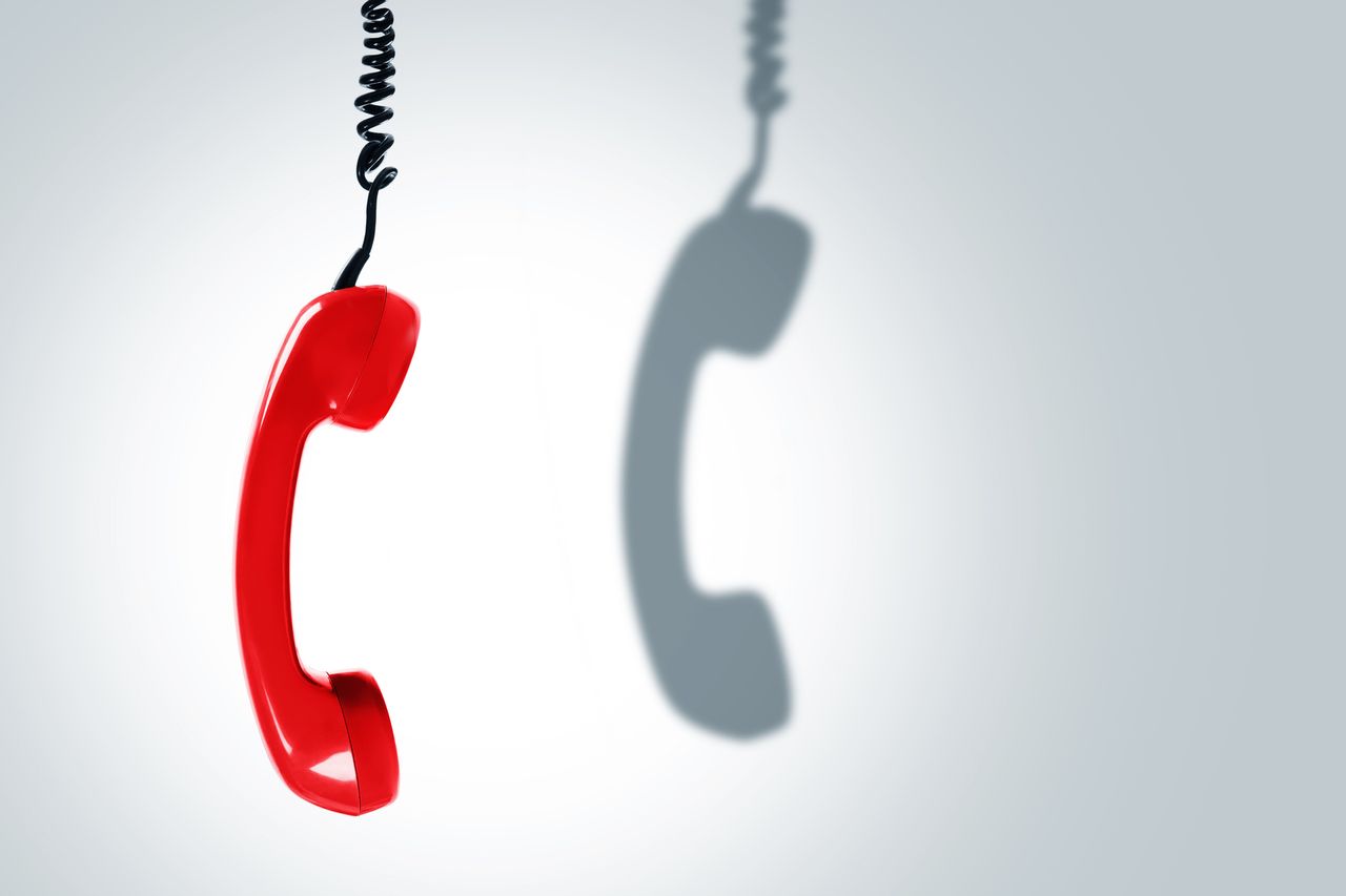 red corded phone dangling with shadow on white backdrop