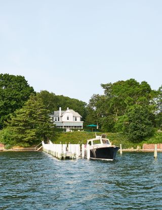 exterior view of island home with white render and jetty with boat and trees all around
