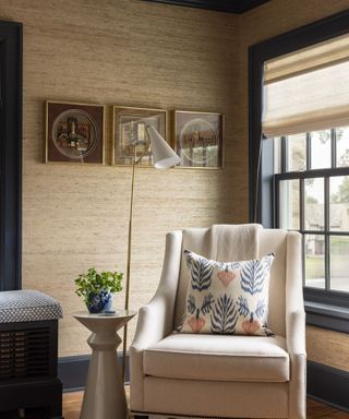 corner of room with beige textured walls, dark blue trim work around window, cream armchair with cushion