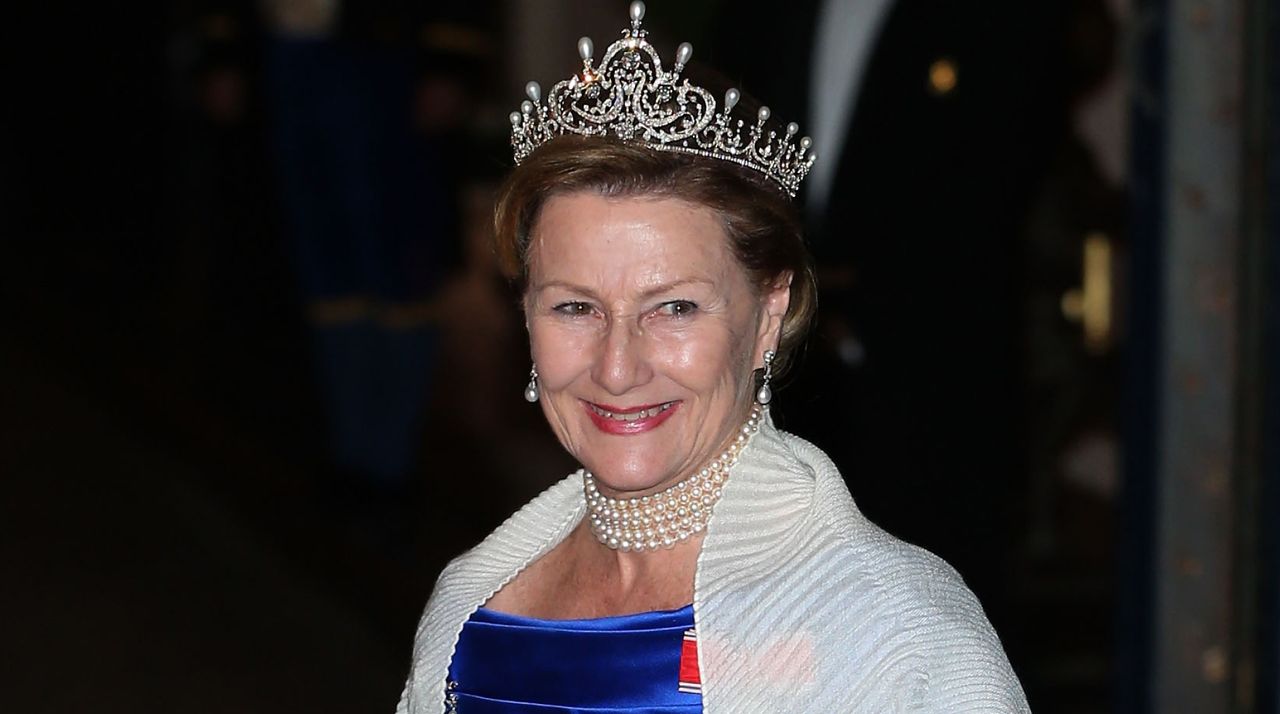 Queen Sonja of Norway wears a royal blue dress, a white shawl, and a diamond tiara