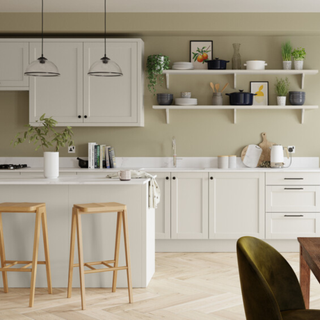 An off-white shaker style kitchen with sage green painted walls and classic cream wall shelves lined with cookware and plants