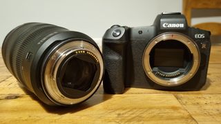 The lens next to a Canon EOS R on a wooden desk