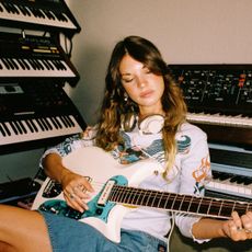 amy allen plays a guitar and sits around a keyboards in a studio