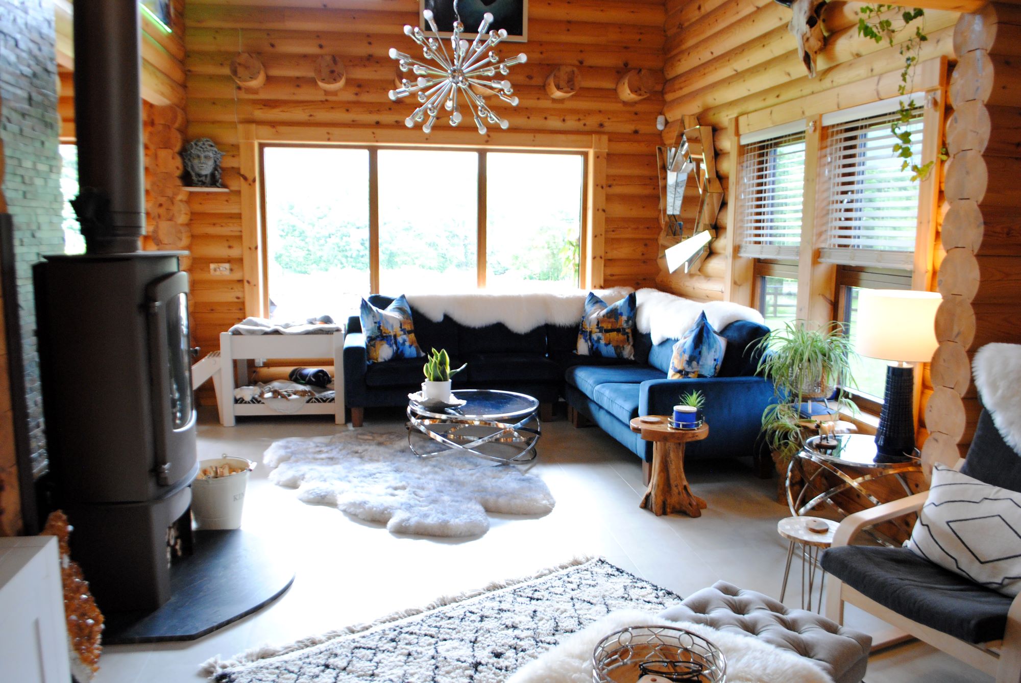 The living room has sofas with fur like coverings and a log burner with large wooden windows and white flooring