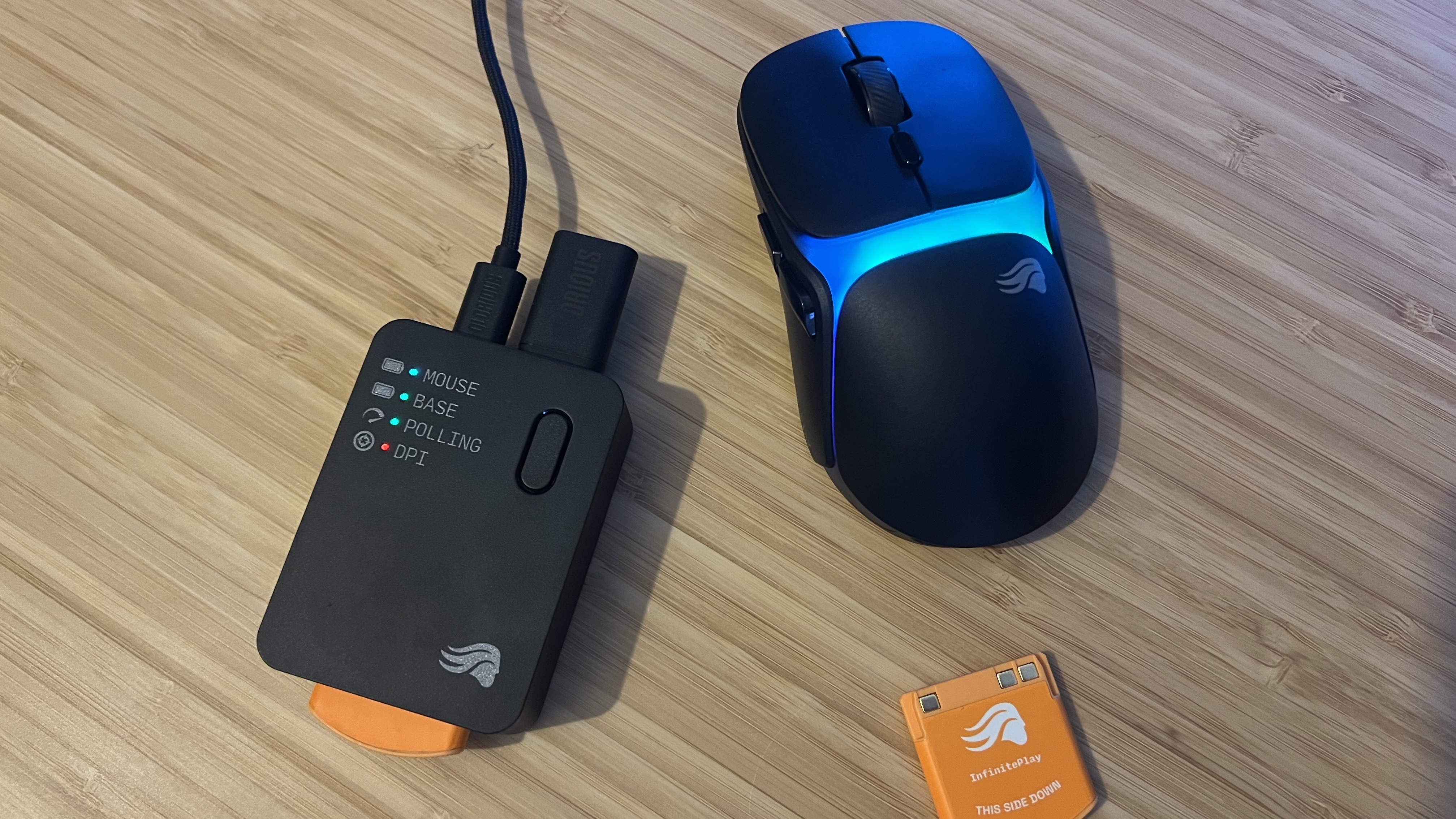 Glorious Model O 3 Wireless with connection dock and spare battery on a wooden desk