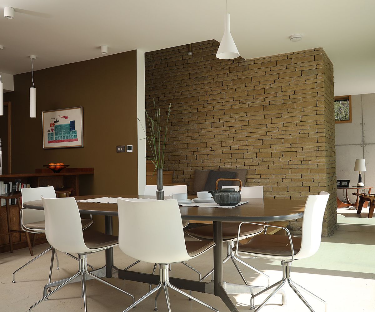 Mid century modern dining table with a brown painted wall and exposed brick wall area