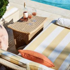 A sun bed next to a pool with a table to the side with a bottle of wine and two glasses on top of the table