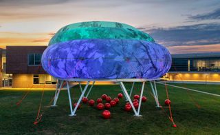 Cloudroom, Ecosistema Urbano, 2021. A blue cloud shaped exhibit on a green lawn with red balls underneath it.