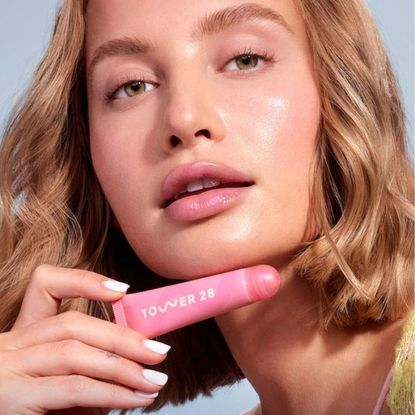 Blonde young woman wearing Tower 28 lip tint and makeup.