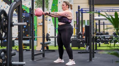 Young larger sized woman working out with kettlebell in gym doing a kettlebell swing