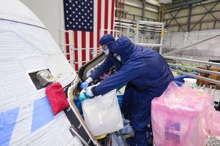 Boeing technicians load a package of mementos aboard the Orbital Flight Test-2 Starliner capsule in preparation for its launch.