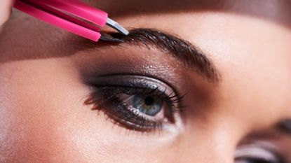 woman plucking her eyebrows with tweezers