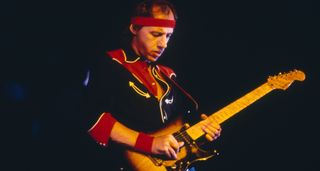 Mark Knopfler plays his Fender Stratocaster live in 1985, wearing a cowboy shirt and red terry headband.
