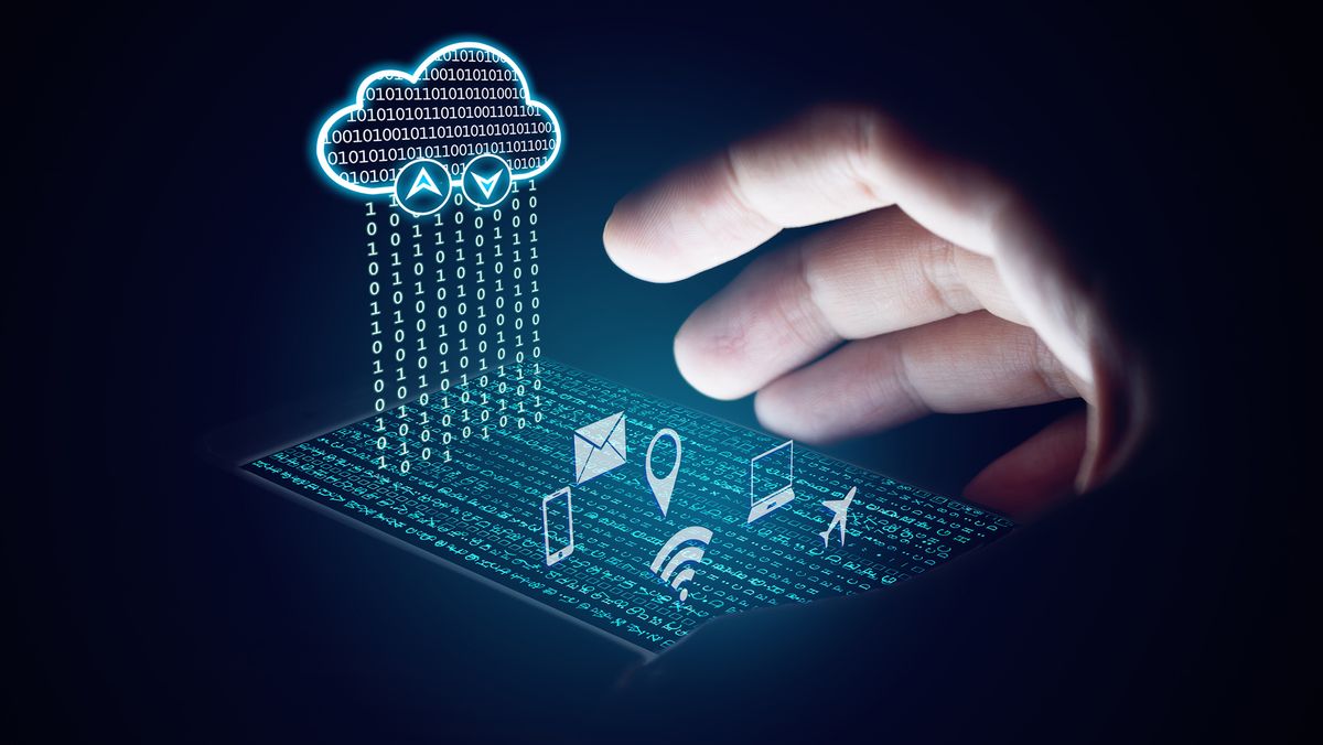 A digital image of a glowing 2D cloud filled with binary code. Binary code is raining down from the cloud onto a digital surface made up of letter that lies perpendicular to it. Popping out of this surface are 2D icons for mail, airplane mode, smartphone, geolocation, WiFi and laptop. A real hand is reaching out to grab it and the palm and underside of the fingers are illuminated by the graphic. The rest of the hand is in shadow and the background of the image is black.