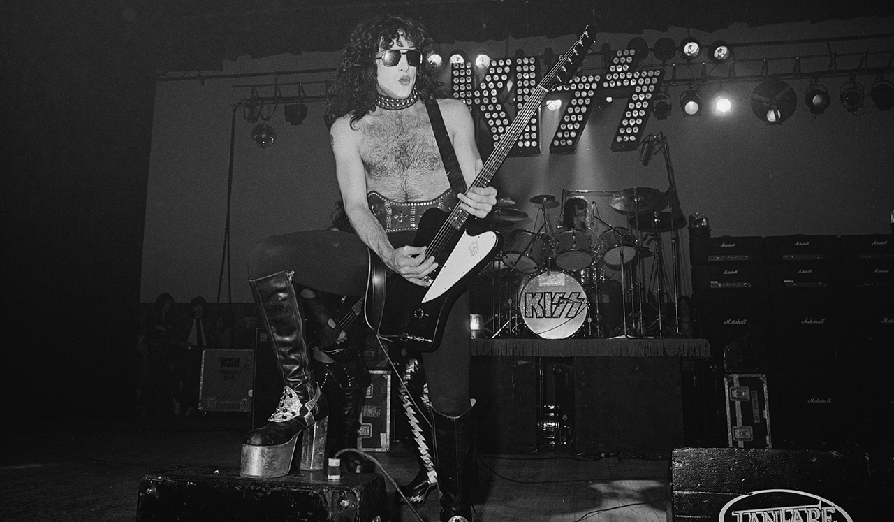 Paul Stanley performs onstage with Kiss – the band's logo bright and lit in the background