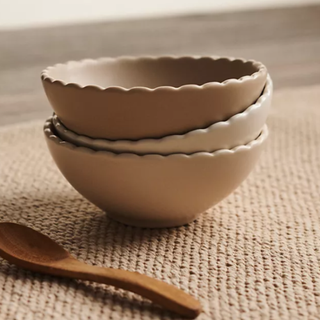 A set of three stacked pinch bowls with a scalloped edge on a jute rug next to a spoon.