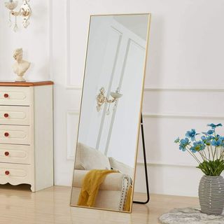 Gold full length standing mirror in a room with a bust, sofa, and flowers