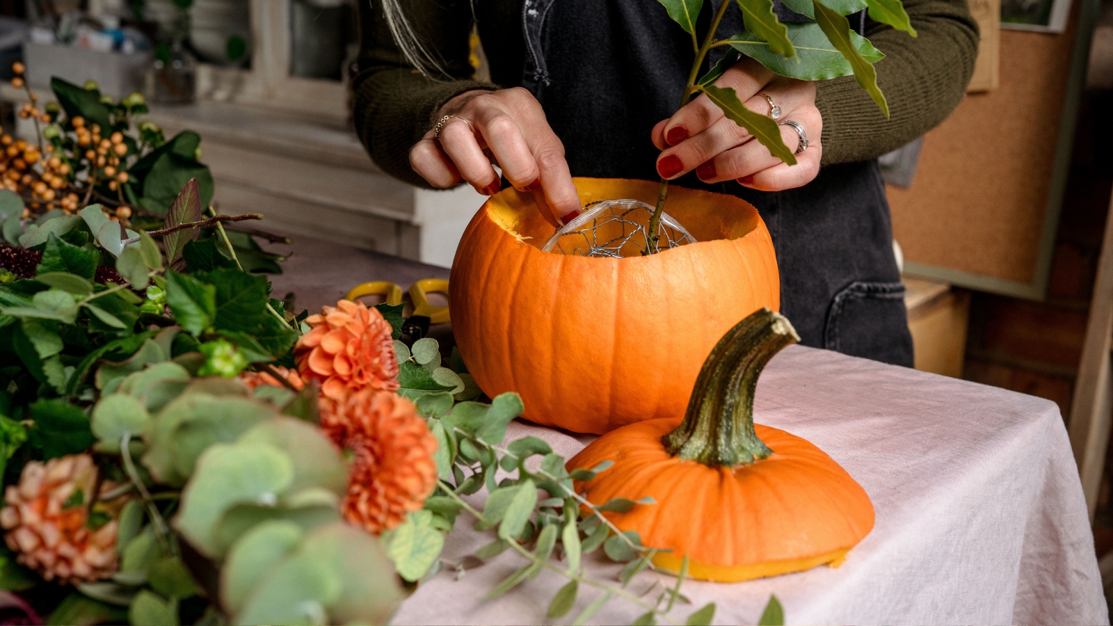Adding a stem of bay into a pumpkin holding chicken wire