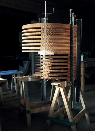 A rocker chair is being assembled. Multiple wooden plates are being held together by a cramp at the workshop.