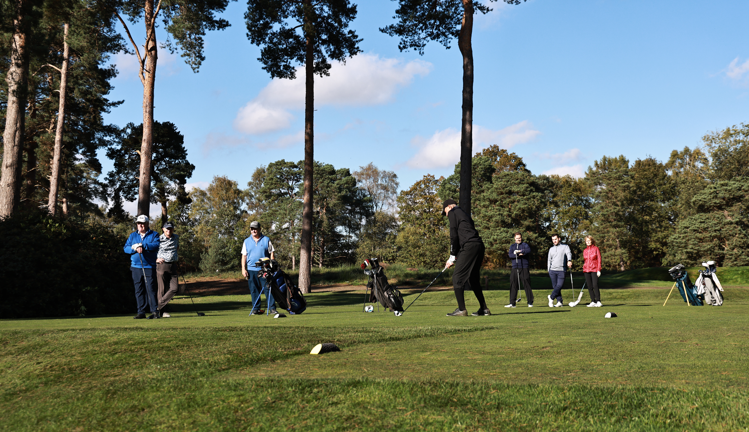 Golfers wait on a tee as a golfer tees off