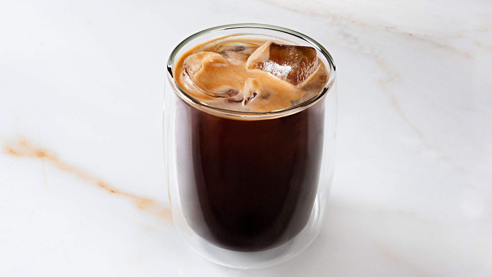 An iced americano in a glass mug on a marble countertop