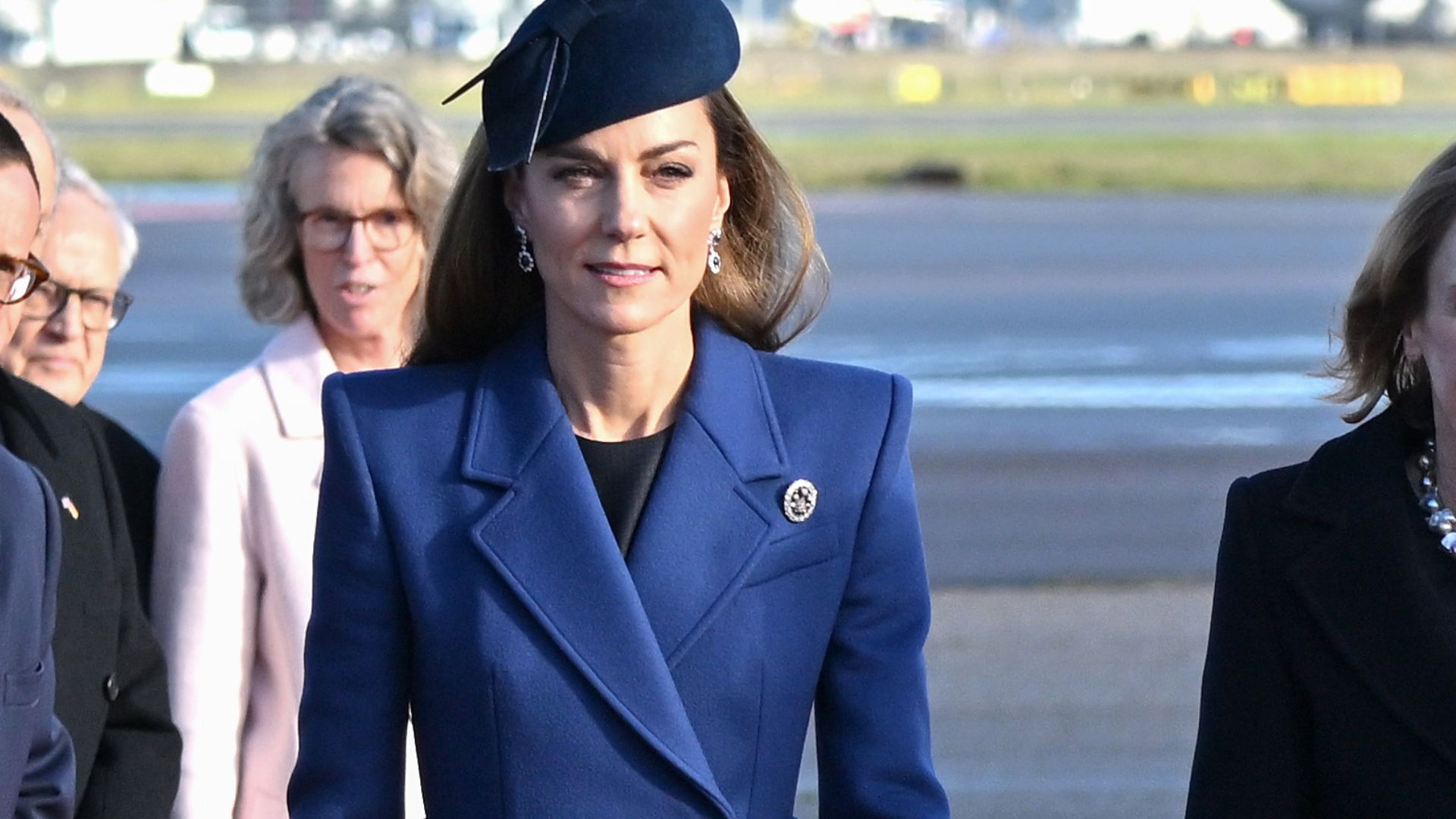 Kate Middleton wears a navy coat with navy suede boots and a navy fascinator.
