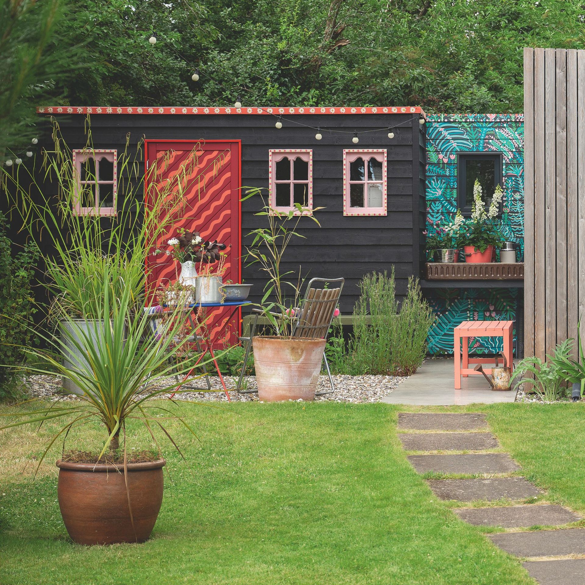 Wooden garden shed with a gravel seating area behind a lawn with plant pot on it