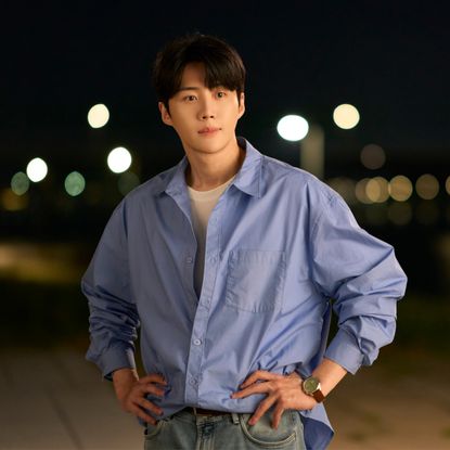 A man in a blue button-down (Kim Seon-ho as Joo Ho-jin) stands on a beach at night, in the Netflix K-drama 'Can This Love Be Translated?'