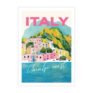 A wall art print with a painted scene of the Amalfi coast with pink buildings, green hills, and a blue ocean with pink writing that says 'Italy' on it