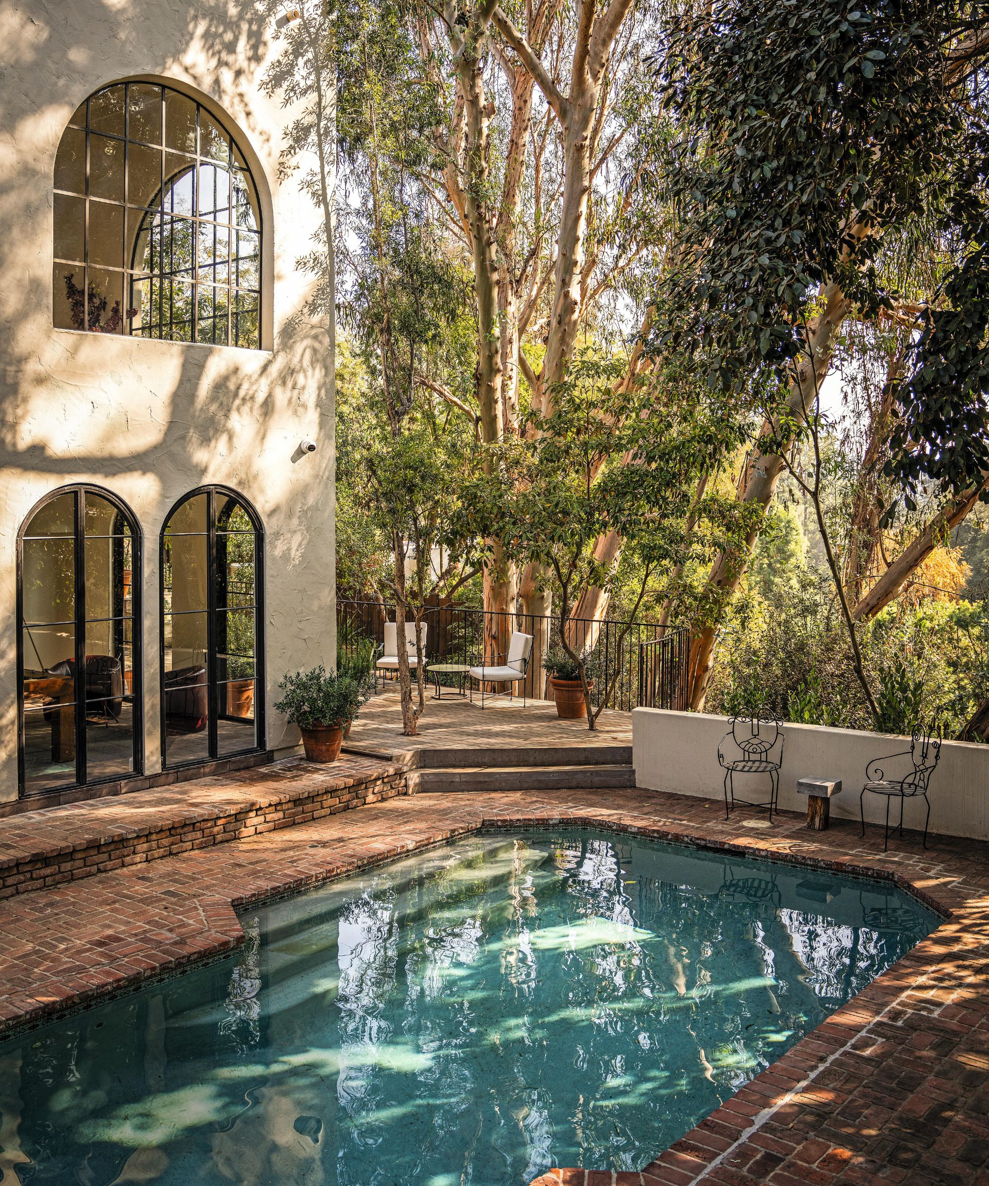 a tree lined LA home with arched windows and a brick paved pool and patio deck