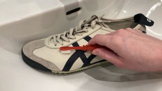A leather white shoe being brushed by a toothbrush in the sink