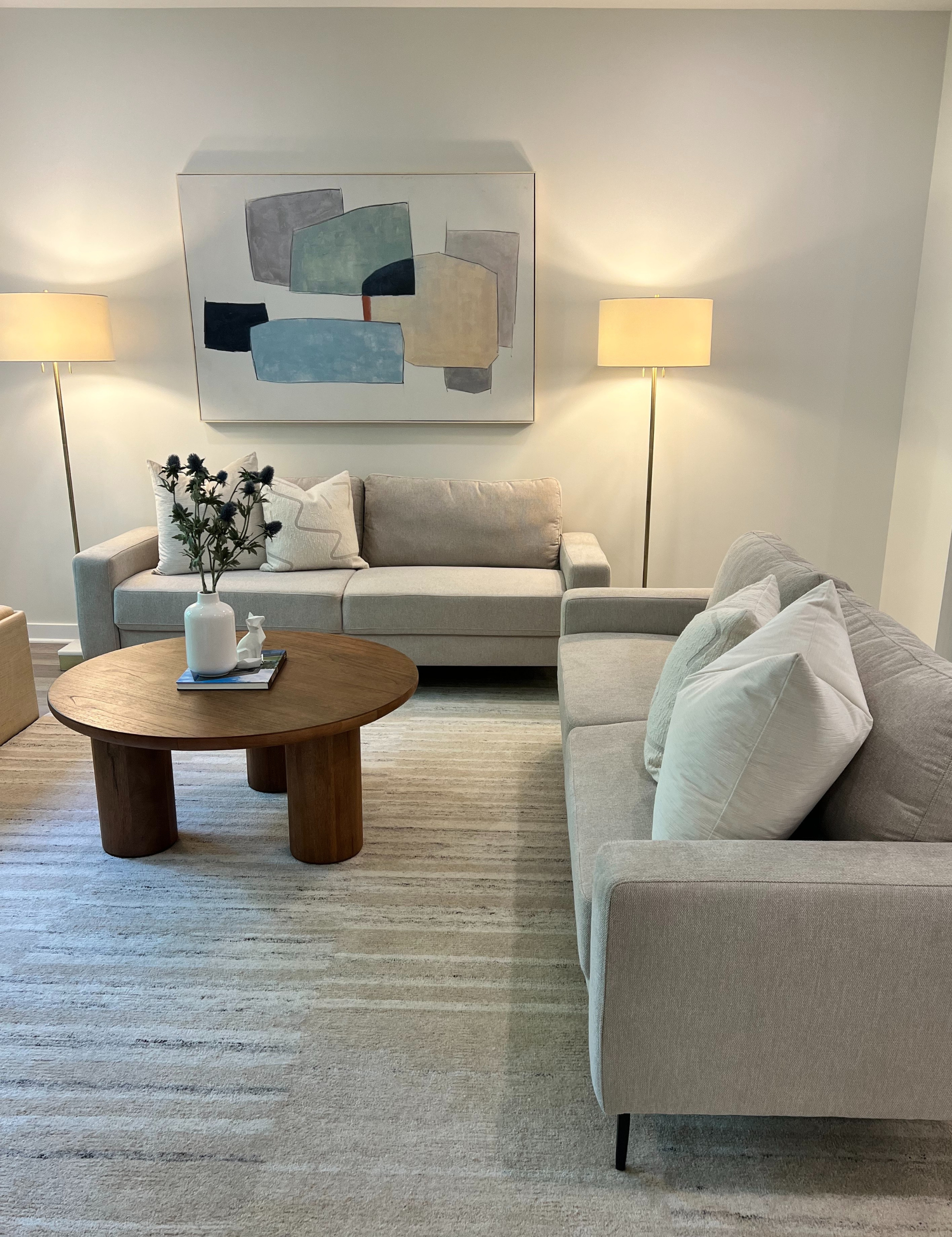 a living room with two sofas, a round coffee table, two floor lamps, and art on the wall above