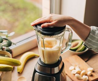 A blender in a countertop with banana and avocado in the background
