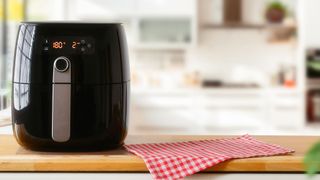 An air fryer on a wooden worktop next to a gingham tea towel