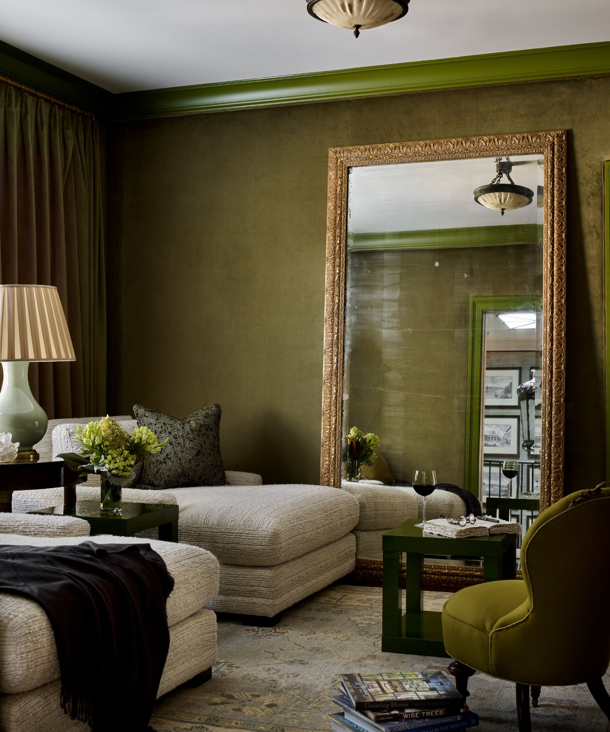 A living room with moss green walls and a large mirror leaning against it.