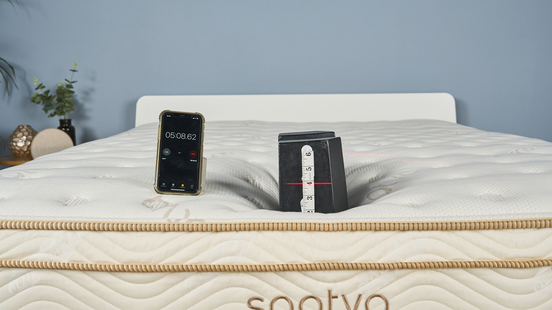 Edge support test using a cast iron 25kg weight on foot of the Saatva Classic mattress, with a stopwatch showing how long the weight compression test has been running for