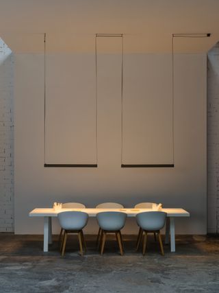 A composition of slim rectangular lights hanging from the ceiling to illuminate a dining table
