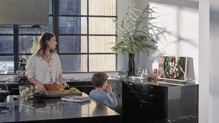 a woman and child looking at the SAMSUNG The Frame QE32LS03TCUXXU 32" Smart Full HD HDR QLED TV in a black and white minimalist kitchen with huge windows behind them